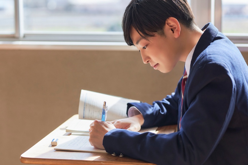 机に向かい、ノートに書き込みながら勉強する高校生